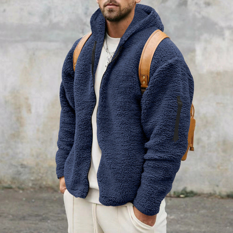 Man wearing navy blue fleece zip-up jacket with tan leather backpack against gray wall