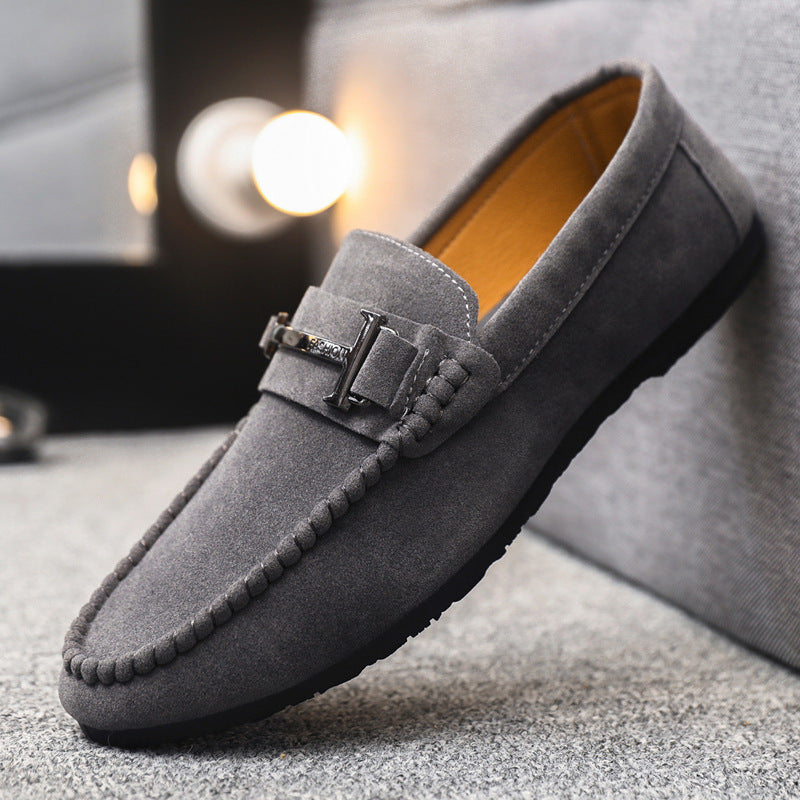 Gray suede men's loafer with decorative metal buckle and braided trim on textured surface