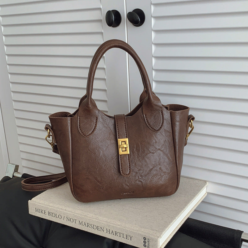Brown leather handbag with gold clasp on a book against white louvered doors