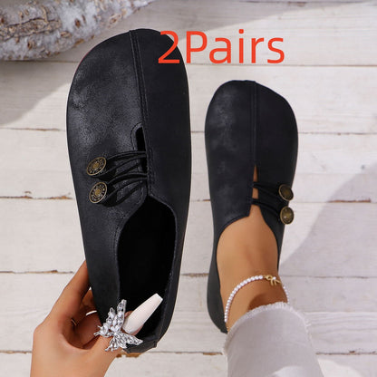 Black slip-on shoes with gold buttons, worn by a person with white pants and pearl anklet