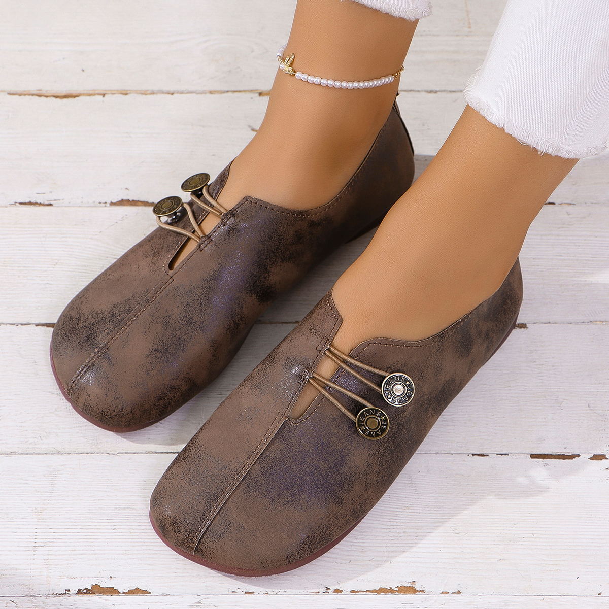 Brown vintage leather slip-on flat shoes with decorative button details on white wooden floor