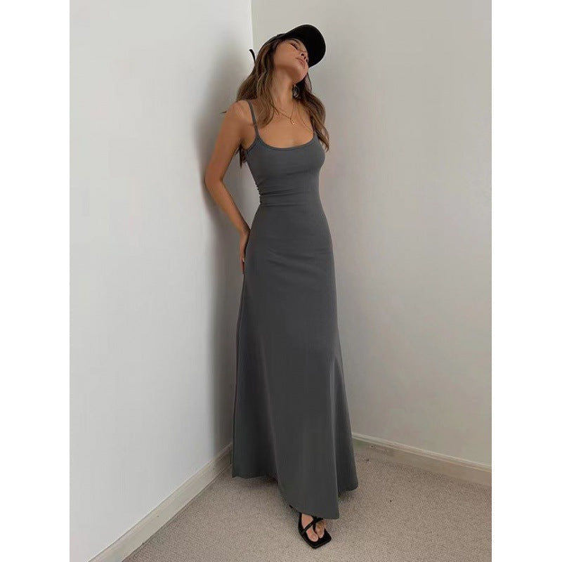 Woman wearing a fitted charcoal gray maxi dress and black cap in a minimalist corner setting