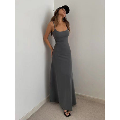 Woman wearing a fitted charcoal gray maxi dress and black cap in a minimalist corner setting