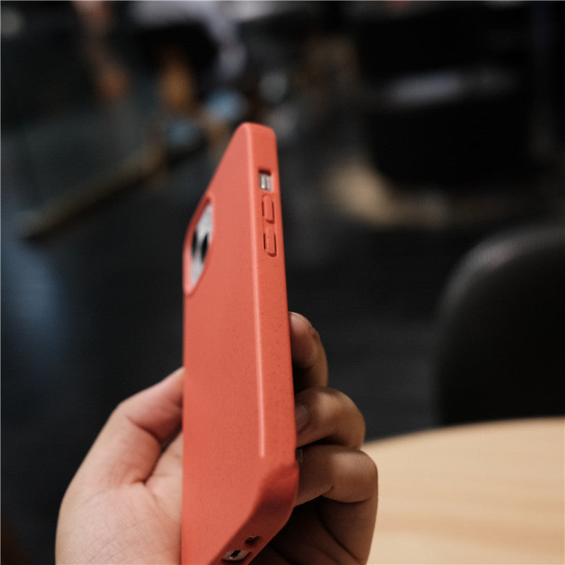 Hand holding coral-colored phone case with camera cutout in blurred indoor setting