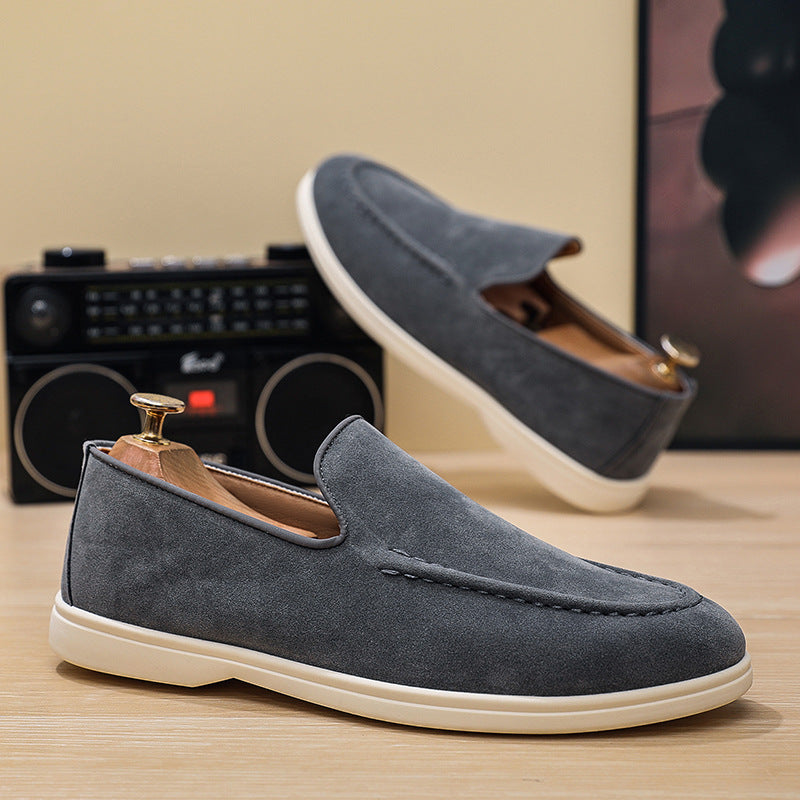 Pair of grey suede slip-on loafers with white soles on wooden surface, retro radio background