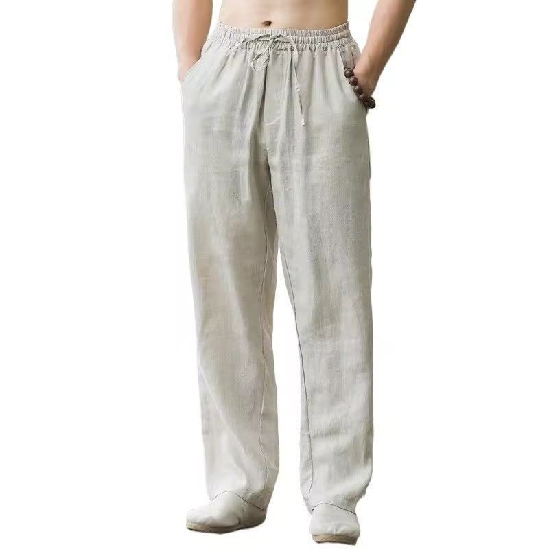 Men's beige linen drawstring pants with pockets and relaxed fit, styled with a beaded bracelet