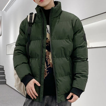 Person wearing a dark green puffer jacket over a black patterned sweater in a modern indoor setting