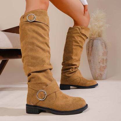 Tan suede knee-high boots with silver buckle straps on model against neutral background