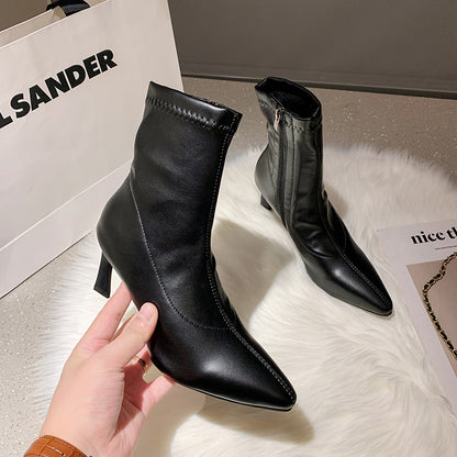 Black leather pointed-toe ankle boots with heels, displayed on white faux fur with a Jil Sander shopping bag