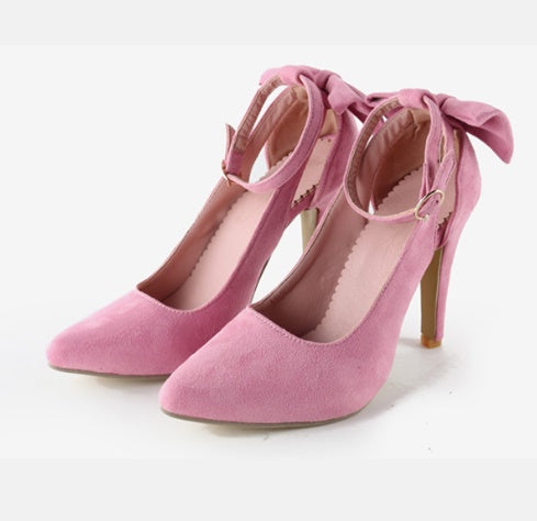 Pair of pink suede high heels with ankle straps and decorative bows on white background