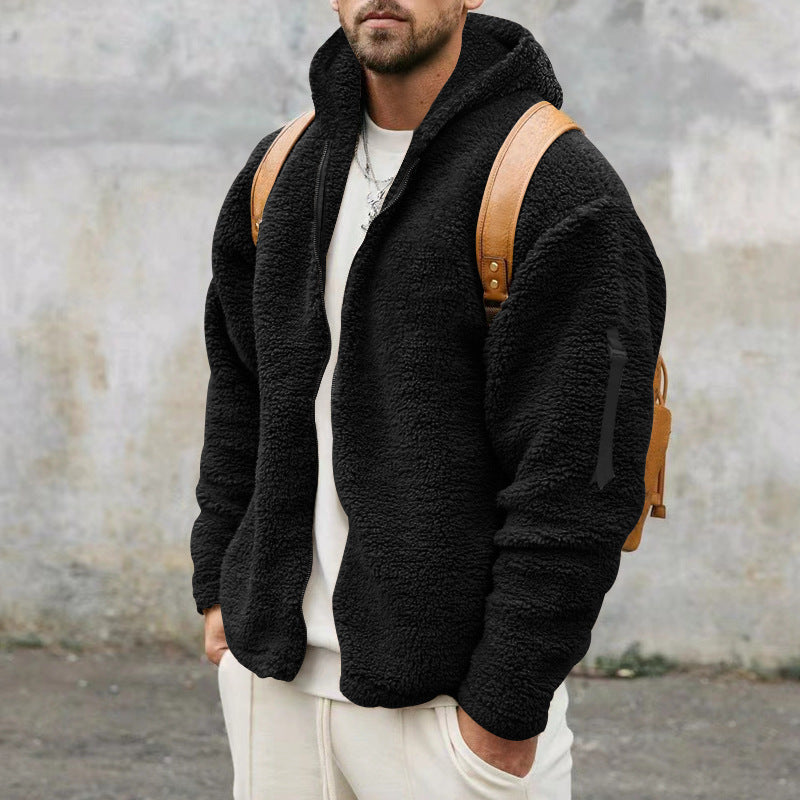 Man wearing black sherpa fleece jacket with hood, white shirt, beige pants, and brown leather backpack outdoors