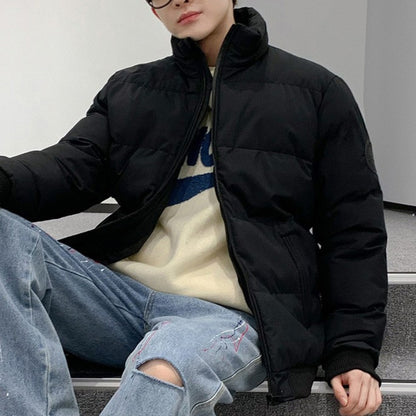 Man wearing black puffer jacket, cream sweater with blue print, and ripped jeans sitting on staircase indoors