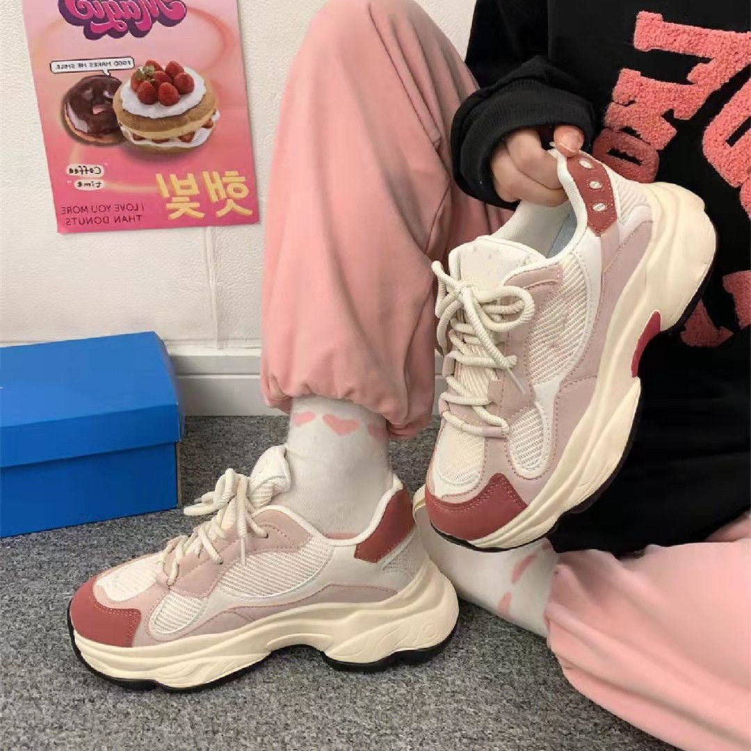 Person wearing pink sweatpants and white-pink chunky sneakers sitting on gray carpet near blue shoebox and dessert poster