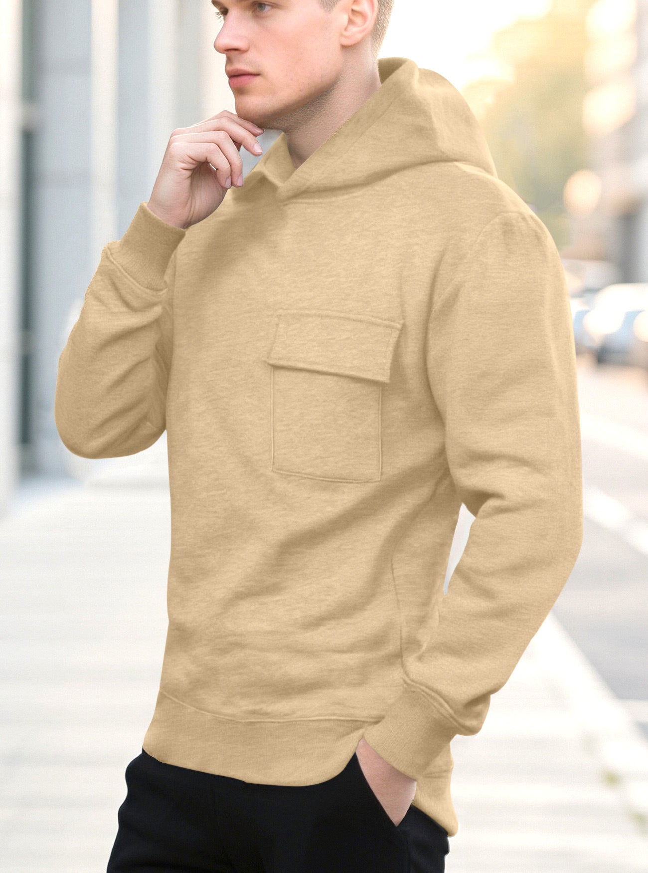 Young man wearing beige hoodie with front pocket and black pants outdoors in urban setting
