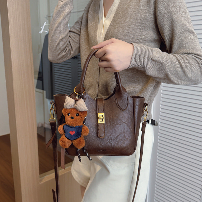 Woman holding stylish brown leather handbag with teddy bear keychain accessory