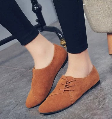 Brown suede lace-up flat shoes worn with black leggings on gray tiled floor