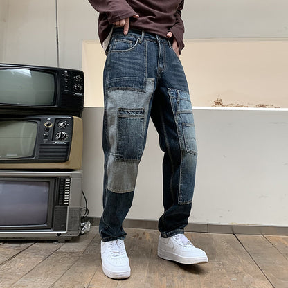 Man wearing patchwork denim jeans and white sneakers standing on wooden floor next to vintage TVs