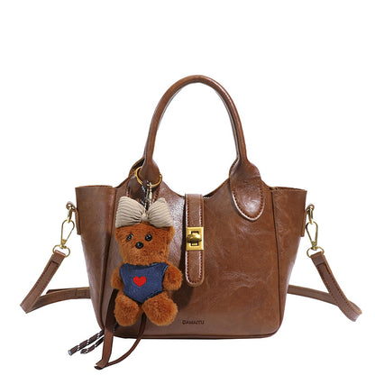 Brown leather handbag with gold lock and detachable straps, decorated with a small teddy bear keychain
