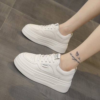 White platform sneakers with thick soles worn by person with tattoo on ankle on gray floor