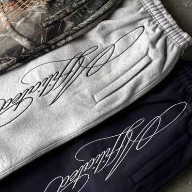 Close-up of gray and black jogger pants with stitched calligraphy design and elastic waistbands