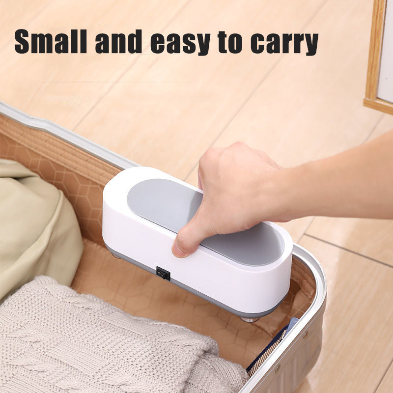 Hand holding small, portable handheld vacuum cleaner over open suitcase with folded clothes