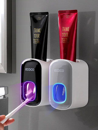 Wall-mounted Ecoco automatic toothpaste dispensers in black and white with LED lights, holding black and red toothpaste tubes labeled Think Your Teeth