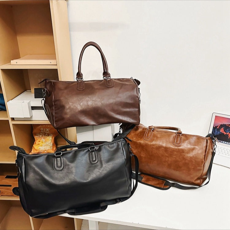 Three leather duffel bags in dark brown, black, and light brown on white table and wooden shelf