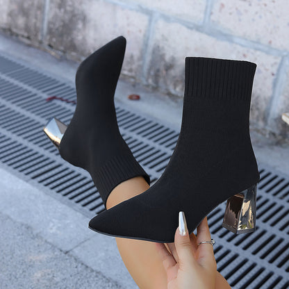 Black sock boots with metallic block heels worn on feet over urban pavement background