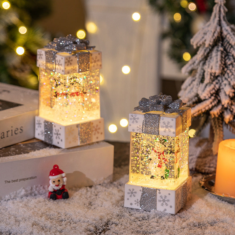 Christmas snow globe gift box decorations with glowing snowman inside, glitter and silver bow on white.