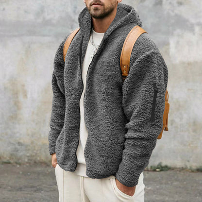 Man wearing gray fleece zip-up jacket with hood and tan leather backpack against concrete wall