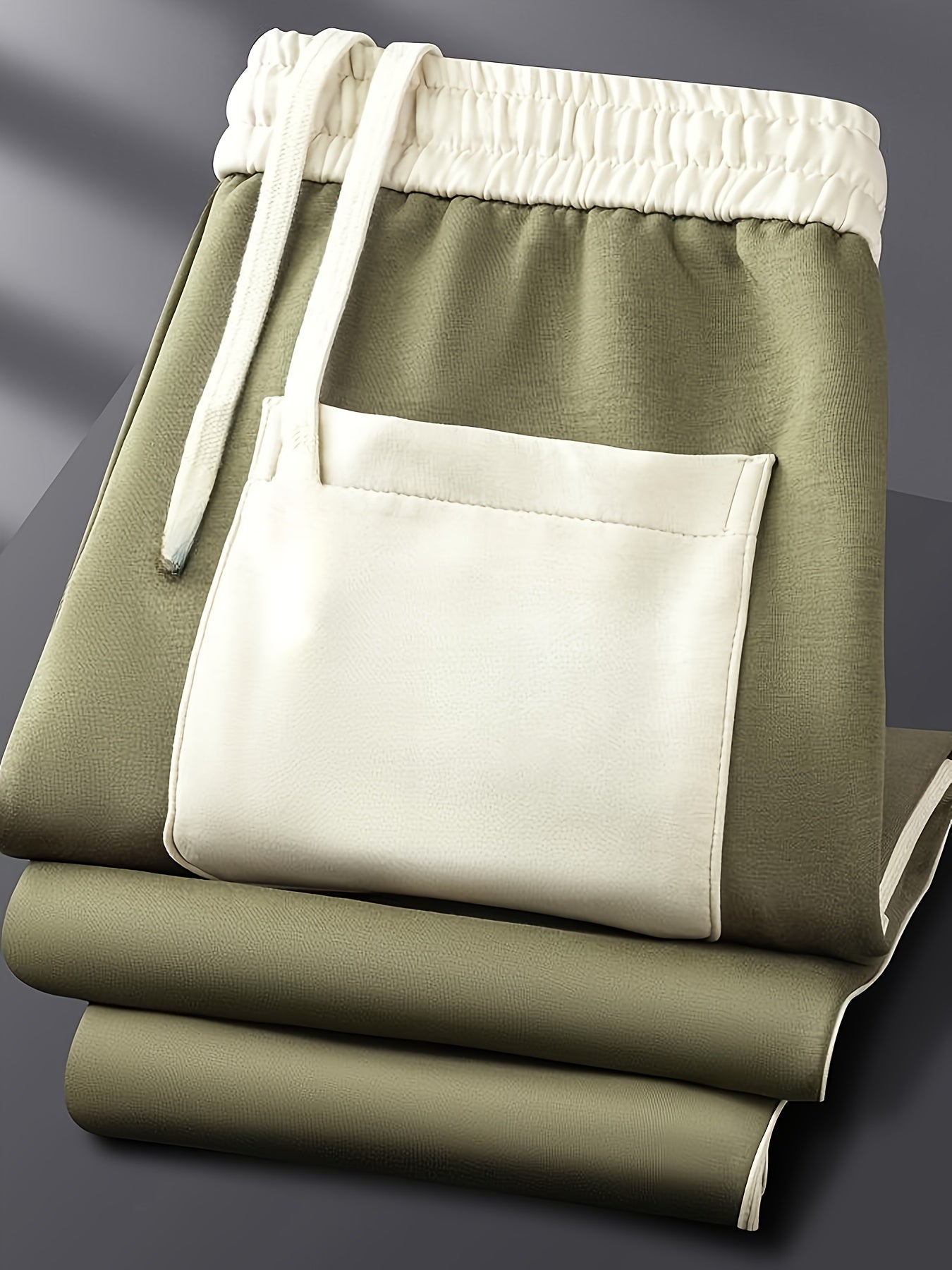 Folded olive green sweatpants with cream elastic waistband, drawstrings, and front pocket