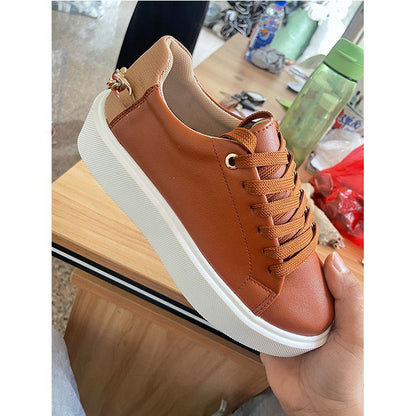 Hand holding brown leather sneaker with beige heel and white rubber sole on wooden table