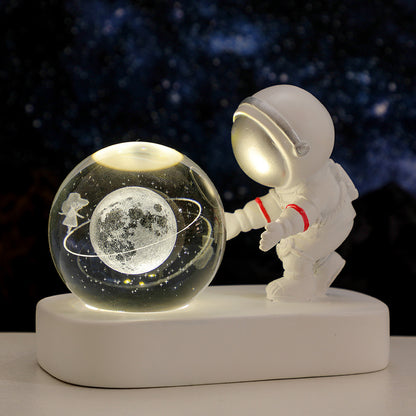 White astronaut figurine touching illuminated glass globe with moon and orbit design on white base