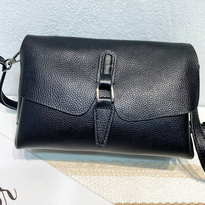 Black textured leather crossbody bag with silver buckle and strap on white surface