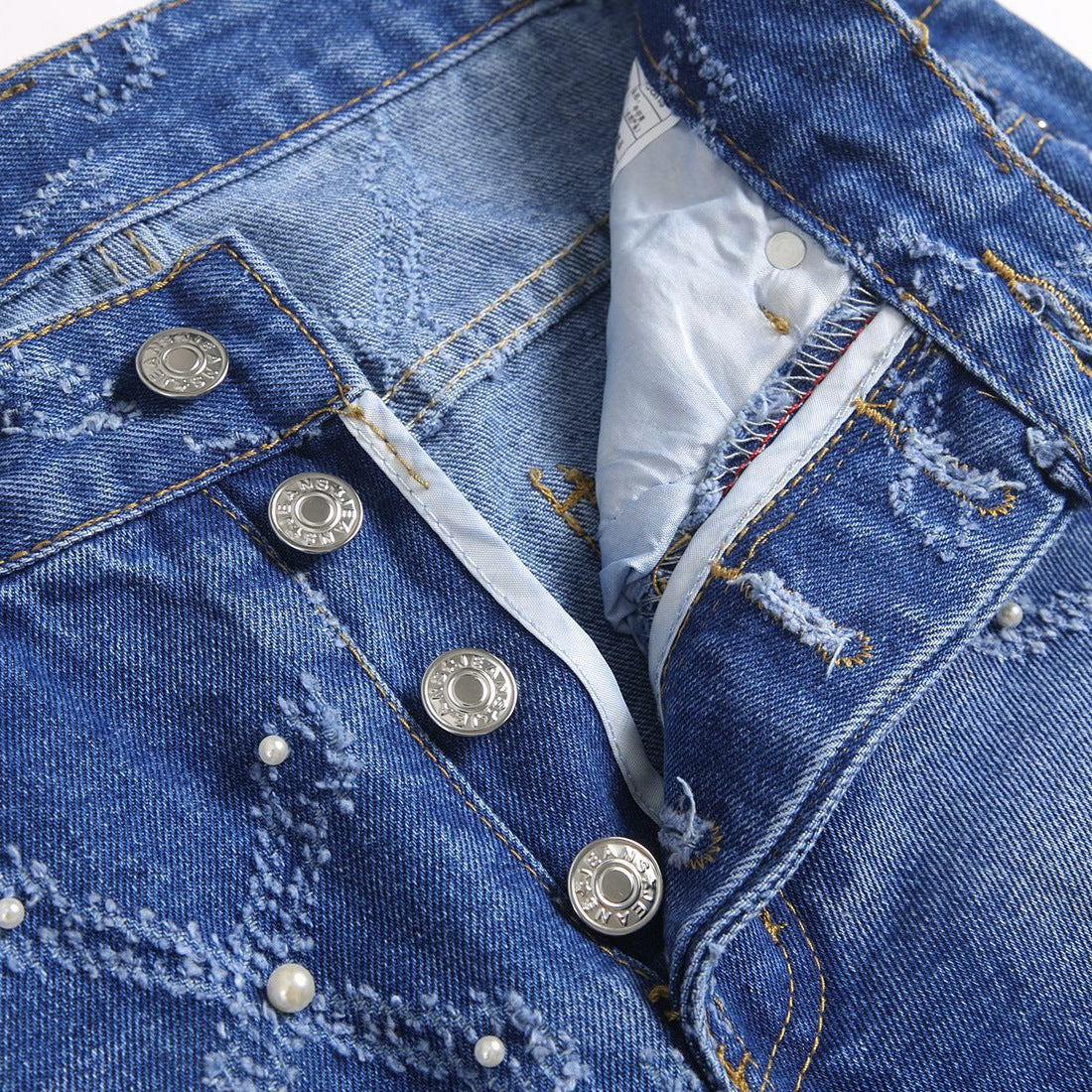 Close-up of blue distressed denim jeans with pearl embellishments and silver branded buttons