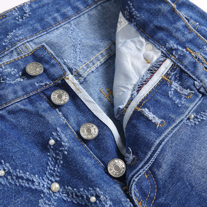 Close-up of blue distressed denim jeans with pearl embellishments and silver branded buttons