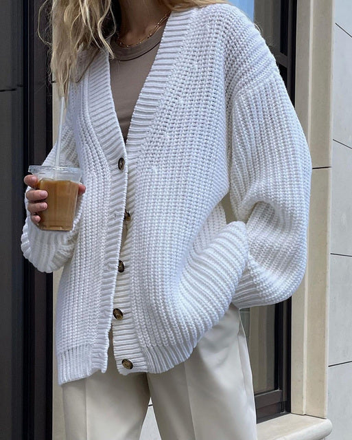Woman wearing white chunky knit cardigan with wooden buttons holding iced coffee outdoors
