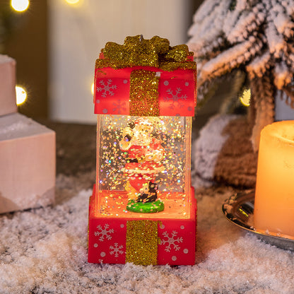 Christmas snow globe with Santa figurine inside a red gift box decorated with gold glitter ribbon and snowflakes