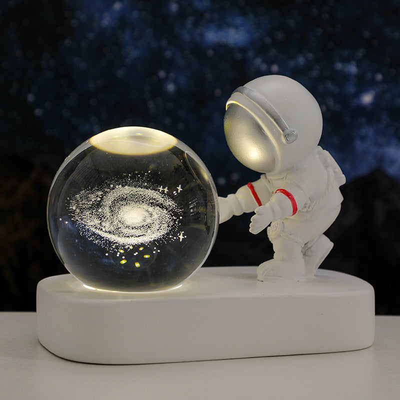 White astronaut figurine touching illuminated glass globe with galaxy design on a white base