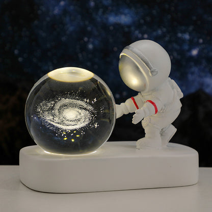 White astronaut figurine touching illuminated glass globe with galaxy design on a white base
