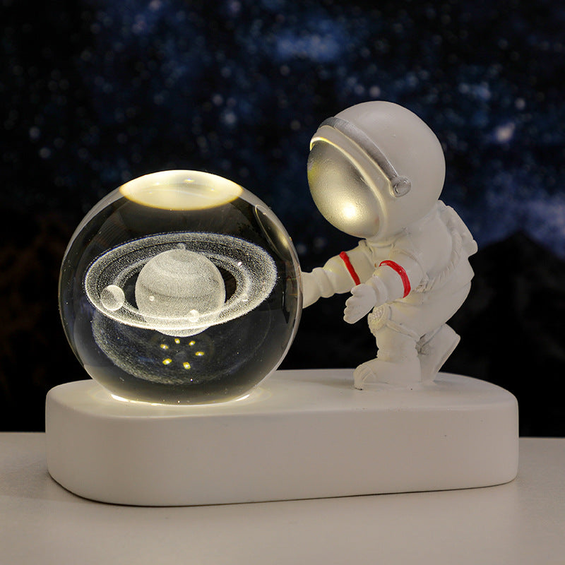 White astronaut figurine touching a glowing crystal ball with Saturn's rings, space decor