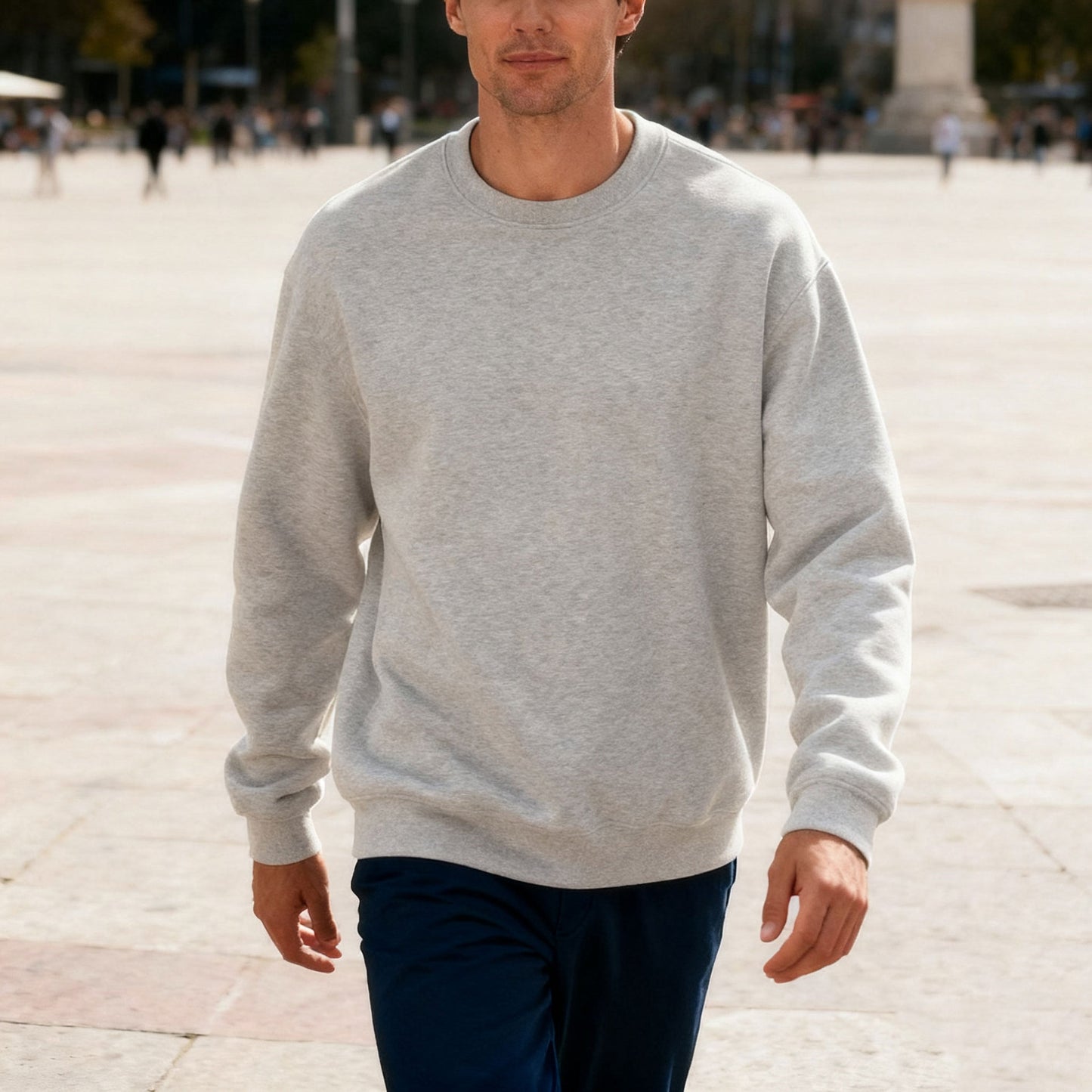 Man walking outdoors wearing a light grey crewneck sweatshirt and dark pants on a sunny day
