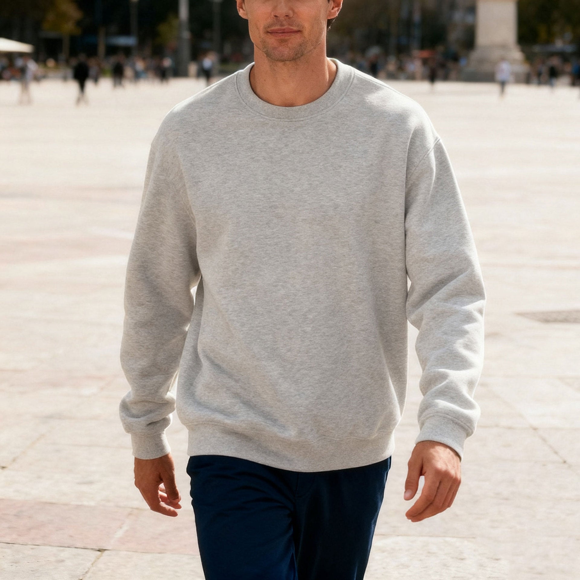 Man walking outdoors wearing a light grey crewneck sweatshirt and dark pants on a sunny day