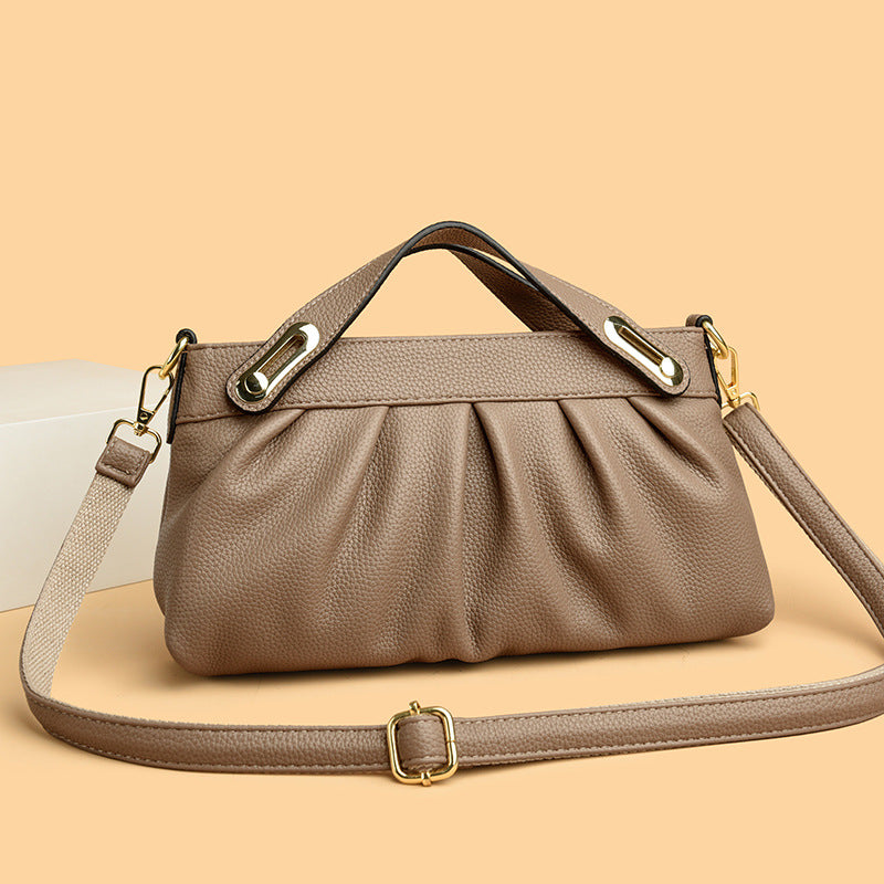Taupe textured leather handbag with gold hardware and detachable shoulder strap on beige background