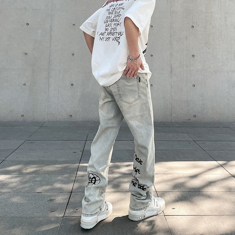 person wearing white graphic t-shirt and light gray jeans with black text designs on concrete pavement