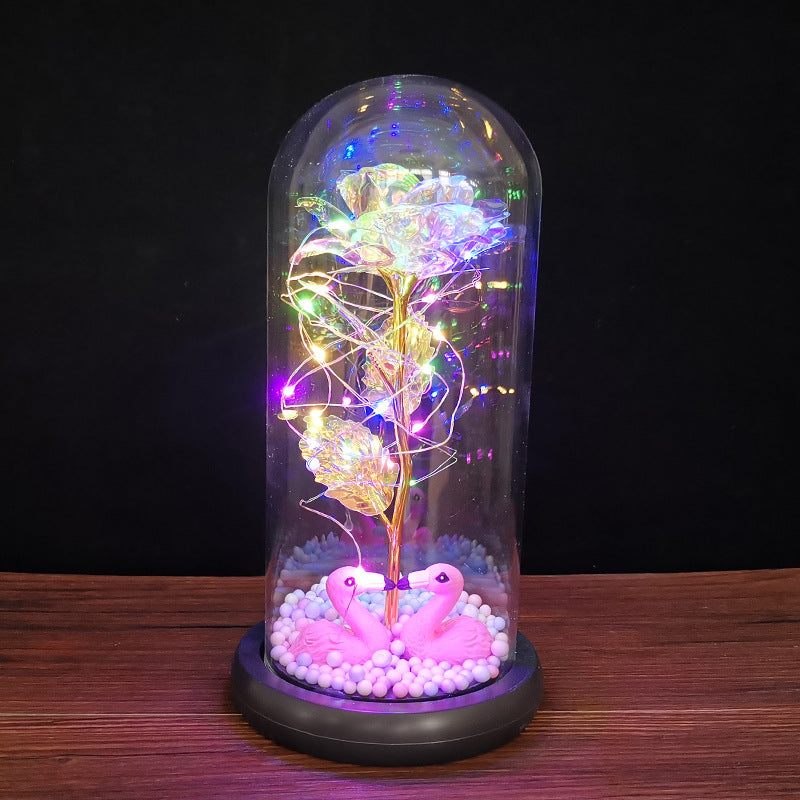 LED light display with golden rose and pink flamingos inside glass dome on wooden surface