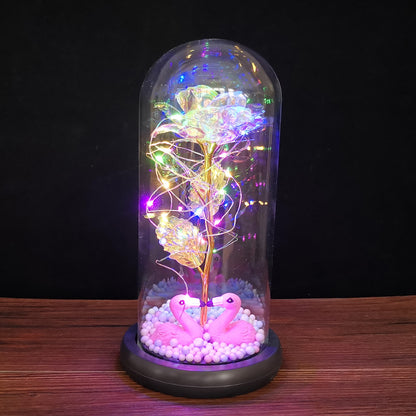 LED light display with golden rose and pink flamingos inside glass dome on wooden surface