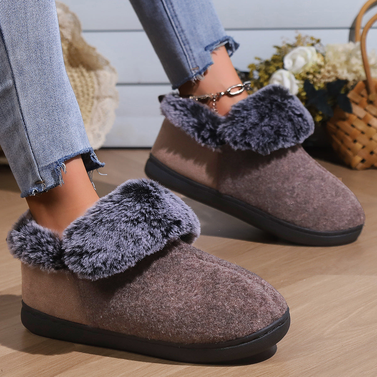 Cozy brown indoor slippers with gray faux fur lining worn with frayed hem blue jeans on wooden floor