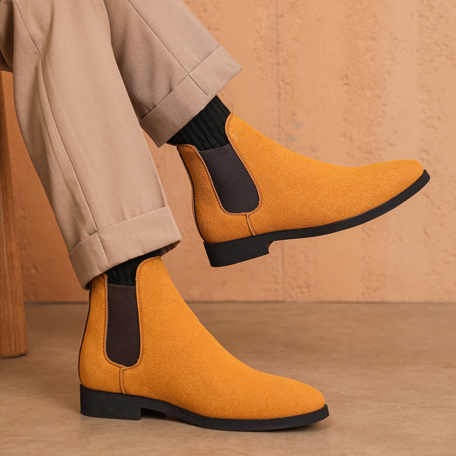 Close-up of mustard yellow suede Chelsea boots with black elastic sides worn with beige trousers