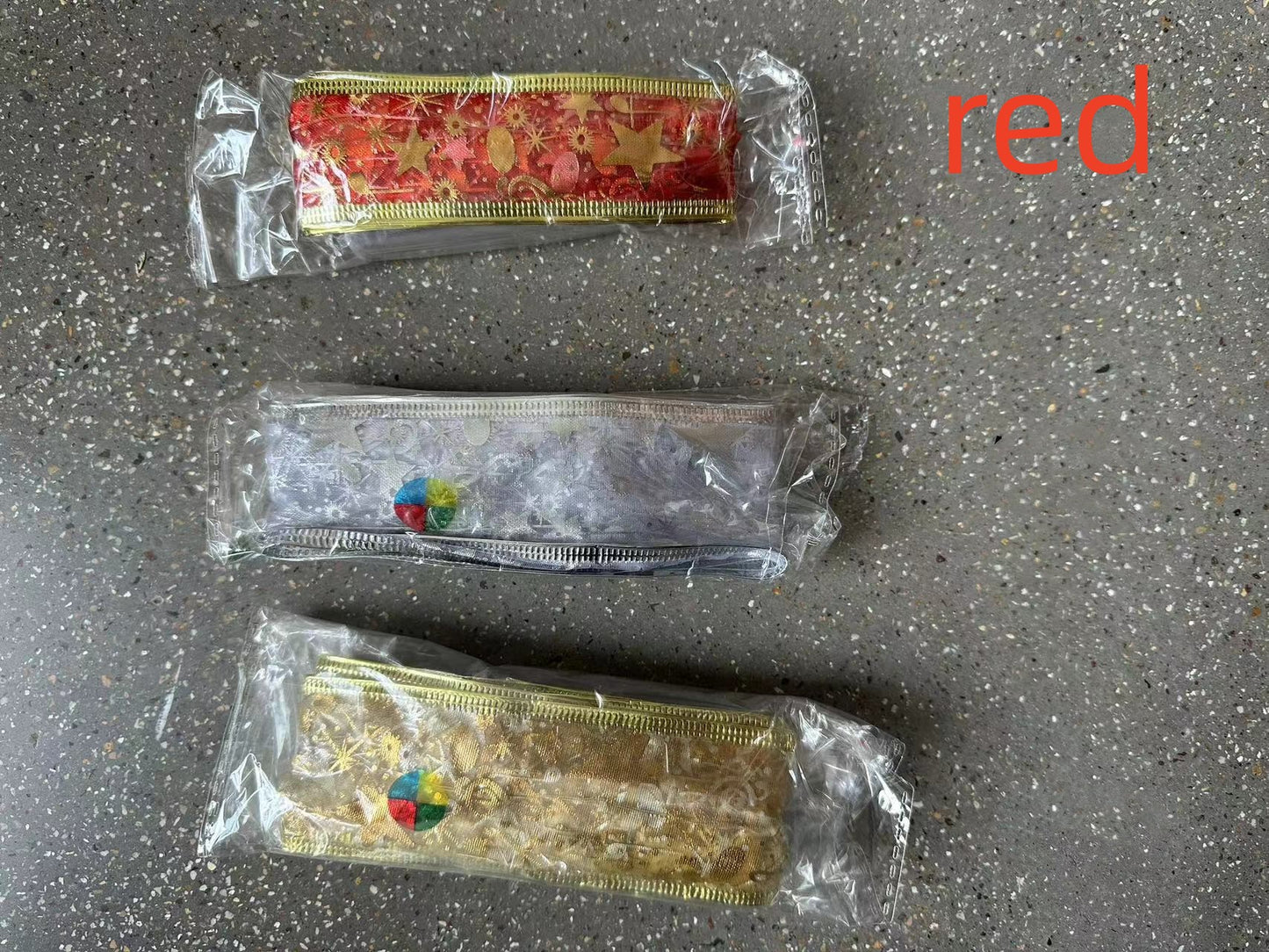 Three decorative metallic ribbon rolls in red, silver, and gold packaging on a speckled surface with red text 'red'